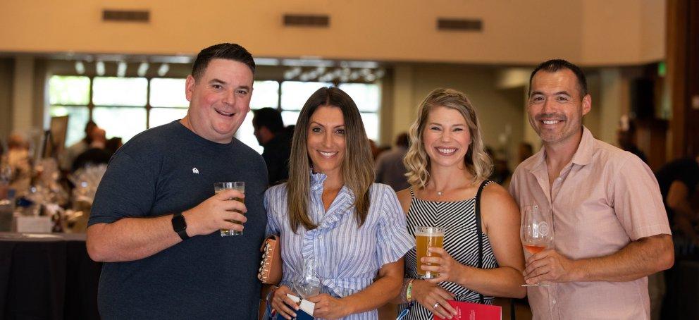 Four people smile while holding beer and wine glasses